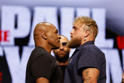 Two men stand side by side, engaged in conversation at a lively boxing event, surrounded by an enthusiastic crowd.